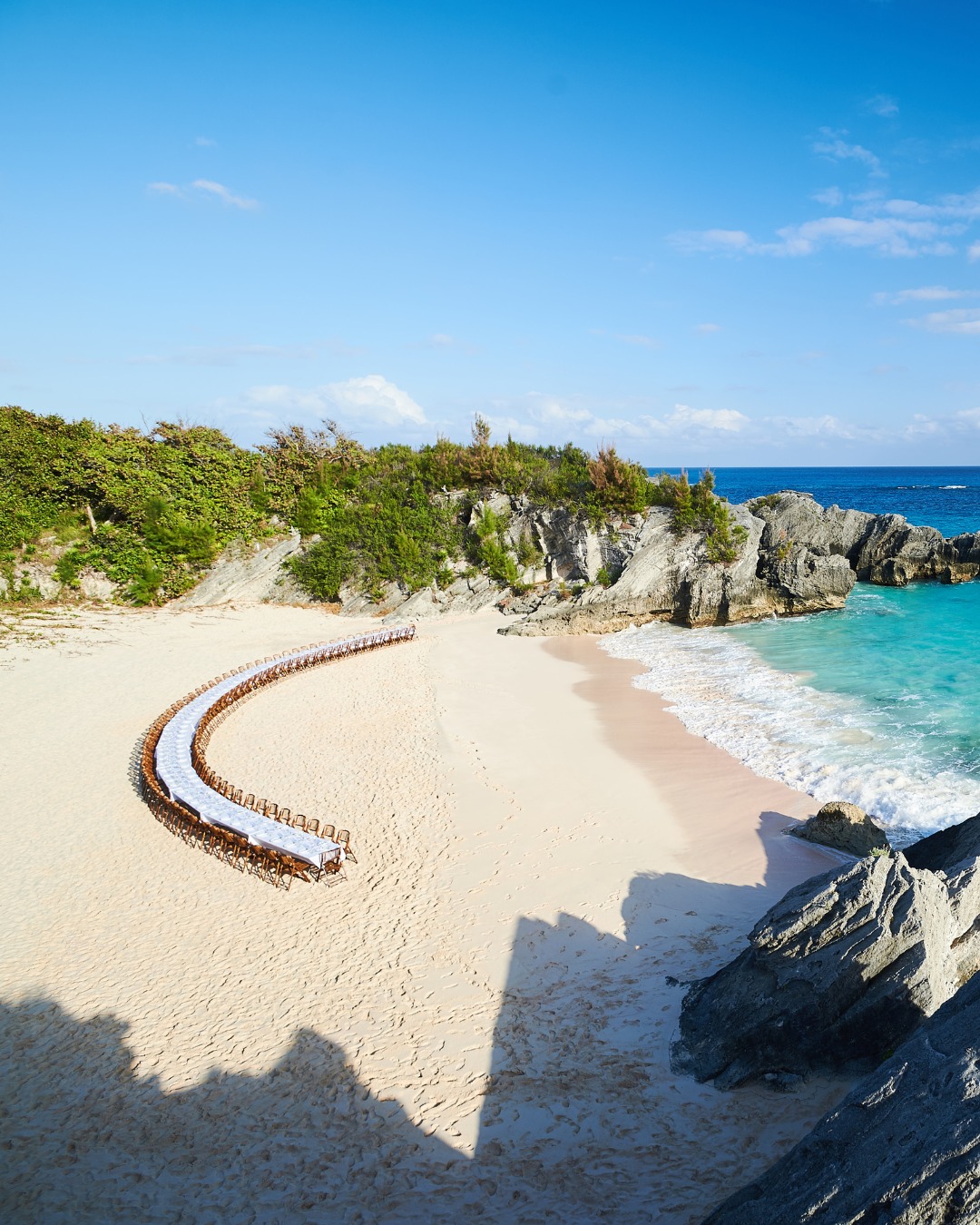 A curved table set on a secluded pink sand cove